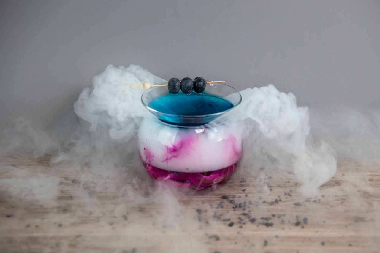 Vibrant cocktail with smoke effect, featuring blueberries and a mystical presentation.
