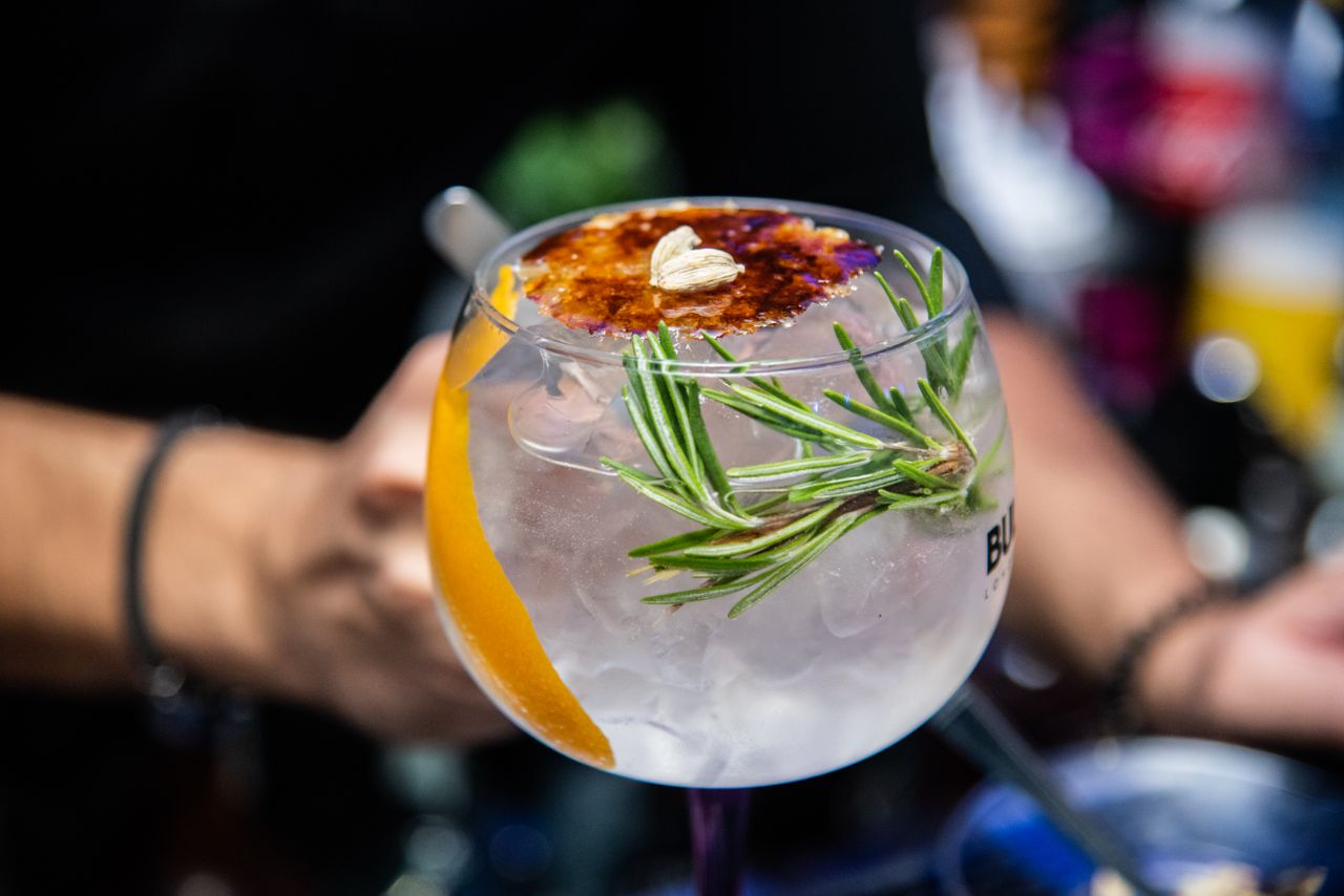 Close-up of an elegant cocktail with citrus and rosemary garnish in a bar setting. Perfect for summer vibes.