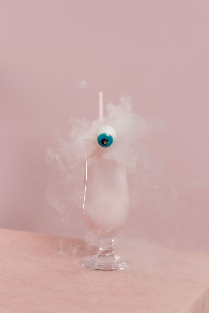 A creative cocktail with an eye decoration and smoke, set in a pink background for a surreal vibe.